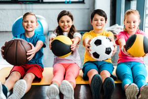 Cheerful kids sitting on fitness mat with balls