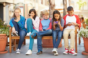 kids on a bench using their cell phones after school.