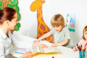 Adult in the kindergarten help to learn child to read letters in early development class. 