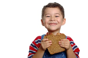 A 5-year-old boy enjoying a sandwich on whole wheat bread.