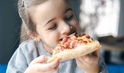 A little girl with a piece of pizza, and the child enjoys eating pizza